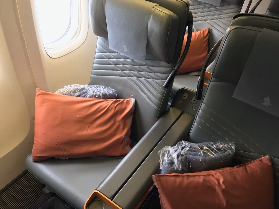 A grey leather premium economy seat with an orange pillow on a Singapore Airlines Boeing 777